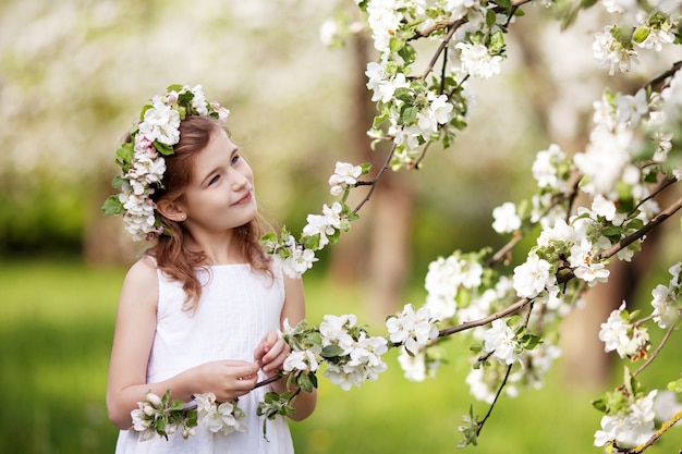 Bella ragazza in abito bianco in giardino con meli in fiore. Ragazza sveglia che tiene ramo di melo