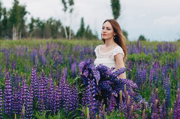 Bella ragazza in abito bianco in piedi tra i lupini