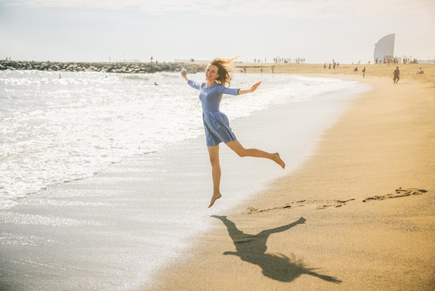 Bella ragazza in abito blu sta camminando sulla spiaggia Incredibile foto estiva Donna che balla e salta vicino al mare Emozioni felici e divertenti Concetto di viaggio per le vacanze Gambe snelle Acqua calda dell'oceano