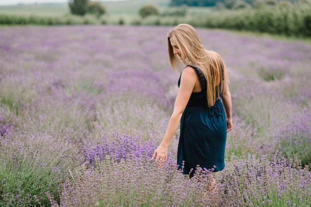 Bella ragazza in abito nel campo di lavanda viola Bella donna a piedi sul campo di lavanda Ragazza raccogliere lavanda Godetevi la natura floreale estate radura Vista posteriore