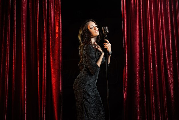 Bella ragazza in abito nero, cantando al microfono nella sala da concerto