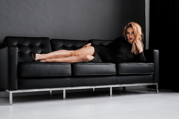 Bella ragazza in abito nero giace sul concetto di lusso divano nero
