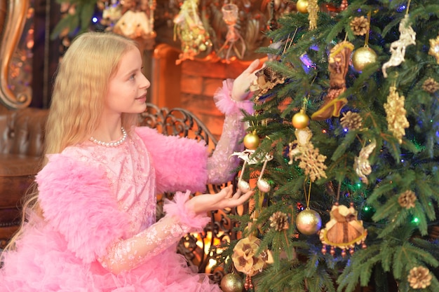 Bella ragazza in abito rosa che decora l'albero di Natale a casa