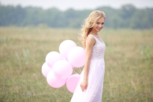 Bella ragazza in abito rosa chiaro con palloncini in mano