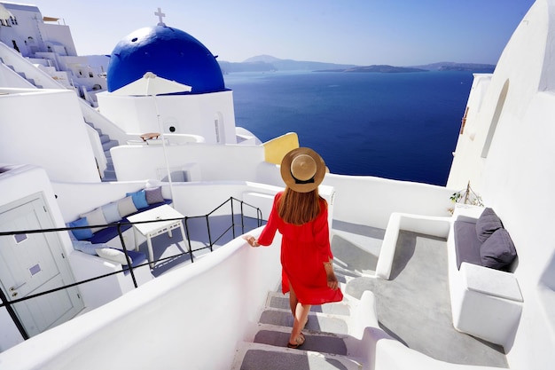 Bella ragazza in abito rosso e cappello scende le scale per il suo resort godendo di una vista spettacolare della Caldera nel villaggio di Oia Santorini Grecia