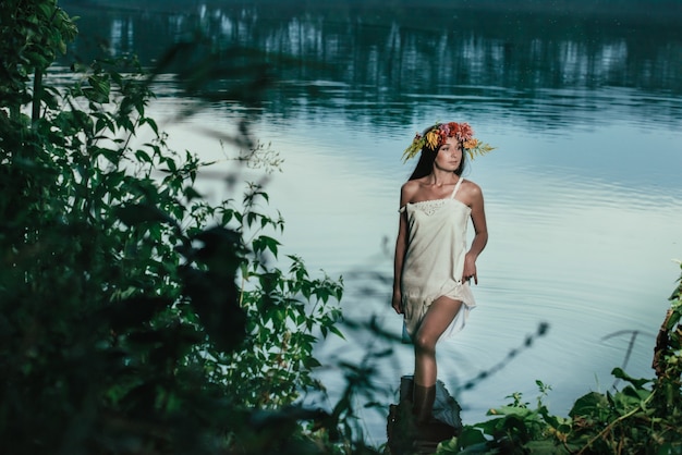 Bella ragazza in abito vintage bianco e corona di fiori in acqua