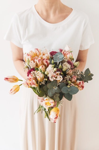 Bella ragazza in attesa in mano bouquet di fiori contro il muro bianco