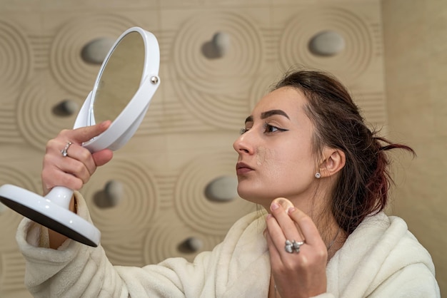 Bella ragazza in camice bianco fa un trucco noioso su uno specchio spazioso Il concetto di trucco stesso