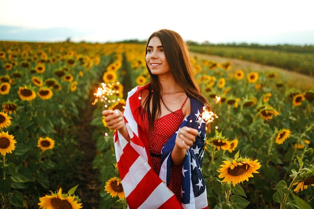 Bella ragazza in cappello con bandiera americana in un campo di girasoli 4 luglio Festa dell'Indipendenza