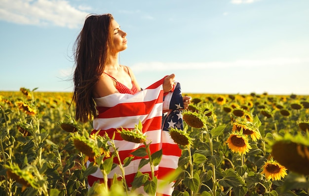 Bella ragazza in cappello con la bandiera americana in un campo di girasoli 4 luglio Quarto di luglio Libertà