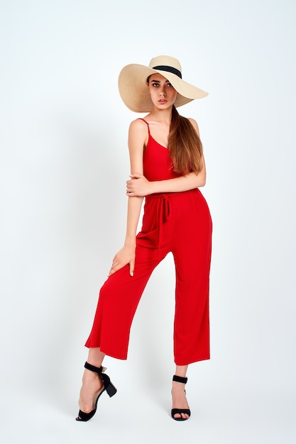 Bella ragazza in cappello da sole in piedi su sfondo bianco in studio in elegante tuta rossa