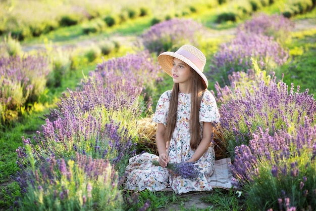 bella ragazza in cappello di paglia e un vestito lungo sul campo di lavanda.