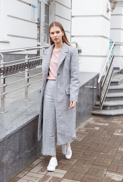 Bella ragazza in cappotto grigio alla moda e pantaloni su sfondo chiaro Camminando per strada