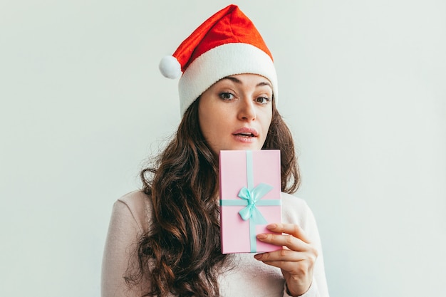 Bella ragazza in contenitore di regalo rosso della tenuta del cappello di Santa Claus isolato