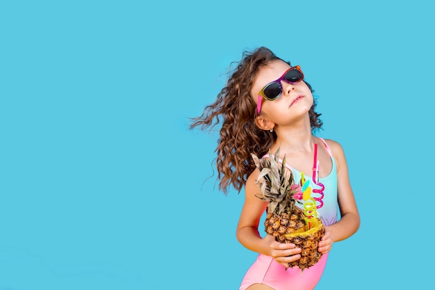 Bella ragazza in costume da bagno colorato e occhiali da sole che tengono pinea