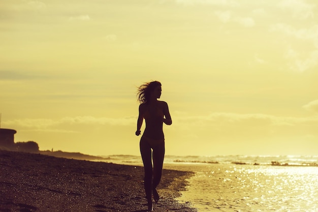 Bella ragazza in costume da bagno giallo che corre sulla spiaggia sabbiosa