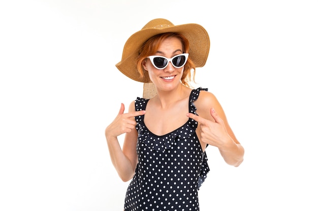 Bella ragazza in costume da bagno retrò e cappello estivo di paglia e occhiali su uno sfondo bianco.