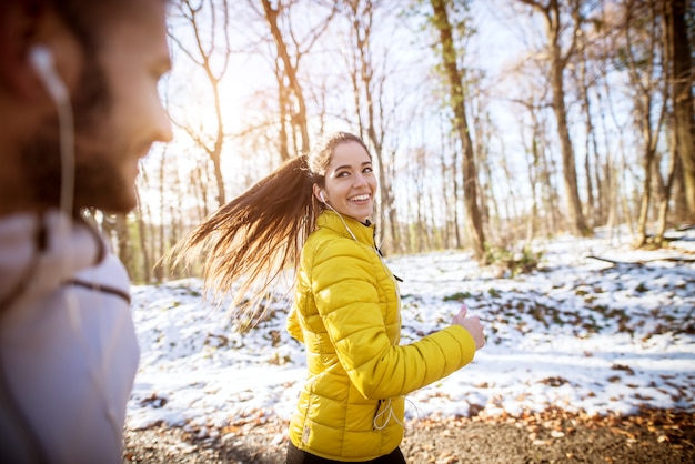 Bella ragazza in giacca gialla in esecuzione accanto a un giovane uomo barbuto nella foresta coperta di neve.