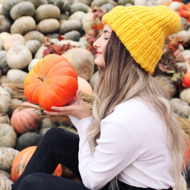 Bella ragazza in giardino d'autunno con zucche gialle