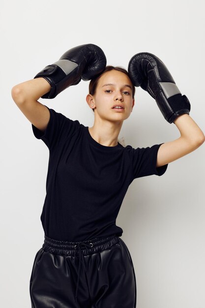 Bella ragazza in guanti da boxe uniformi sportivi neri in posa sullo sfondo isolato