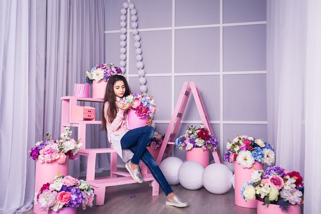 Bella ragazza in jeans e maglione rosa in studio con decorazioni di fiori in cesti.