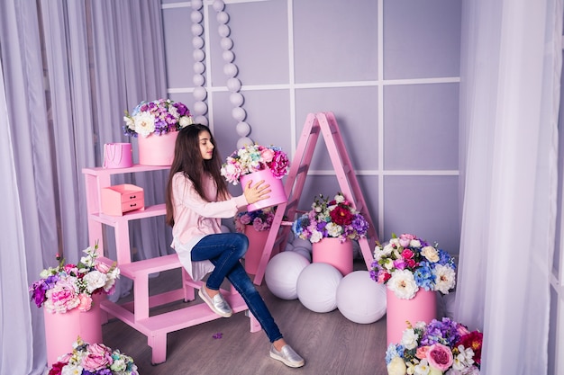 Bella ragazza in jeans e maglione rosa in studio con decorazioni di fiori in cesti.