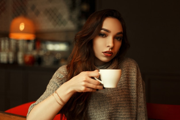 Bella ragazza in maglione lavorato a maglia con una tazza di caffè che riposa in un caffè