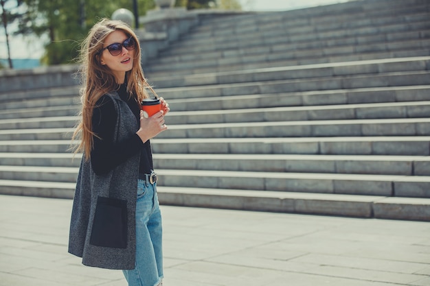 Bella ragazza in piedi sulla strada con caffè e bicchieri.