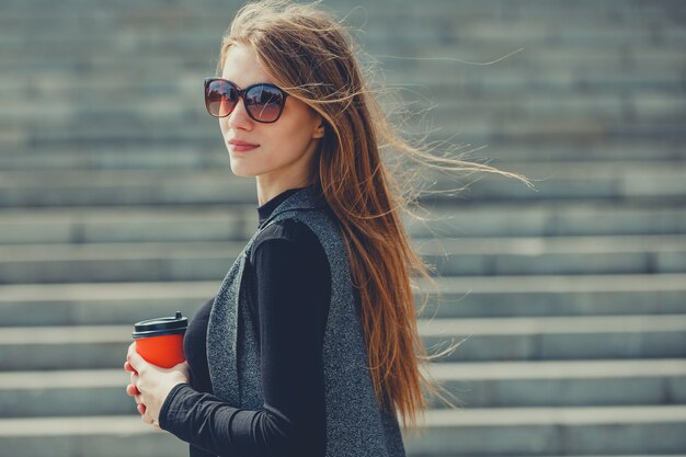 Bella ragazza in piedi sulla strada con caffè e bicchieri.