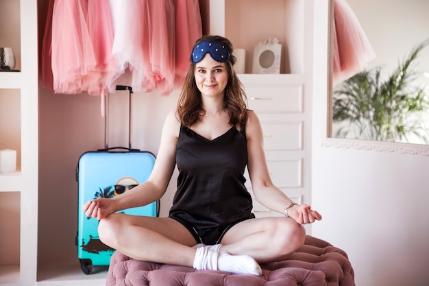 Bella ragazza in pigiama nero al mattino presto pratica yoga nella sua camera da letto. Ragazza seduta in una stanza rosa.