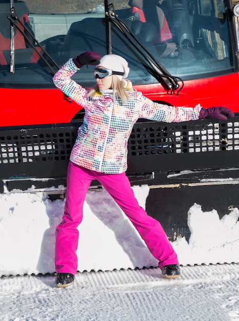 Bella ragazza in posa vicino a spazzaneve in montagna sulla neve