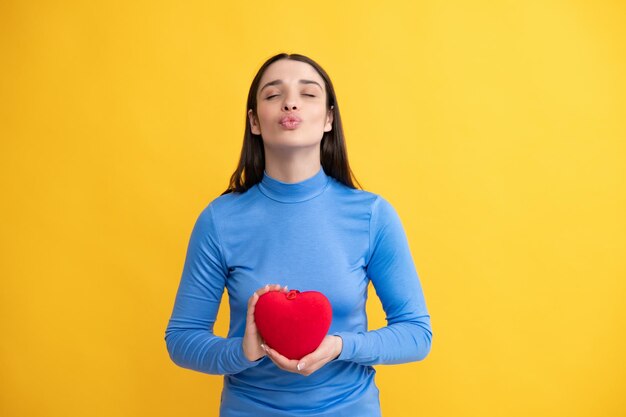 Bella ragazza in possesso di regalo di San Valentino su sfondo giallo Ritratto di giovane donna azienda cuore di carta rossa