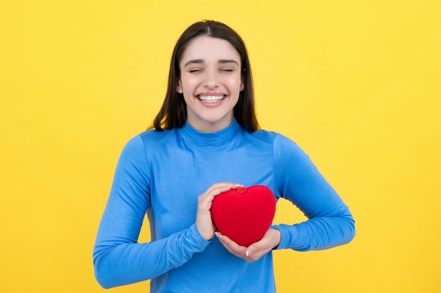 Bella ragazza in possesso di regalo di San Valentino su sfondo giallo Ritratto di giovane donna azienda cuore di carta rossa