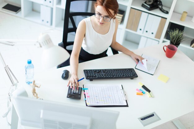 Bella ragazza in ufficio a lavorare con documenti, calcolatrice, blocco note e computer.