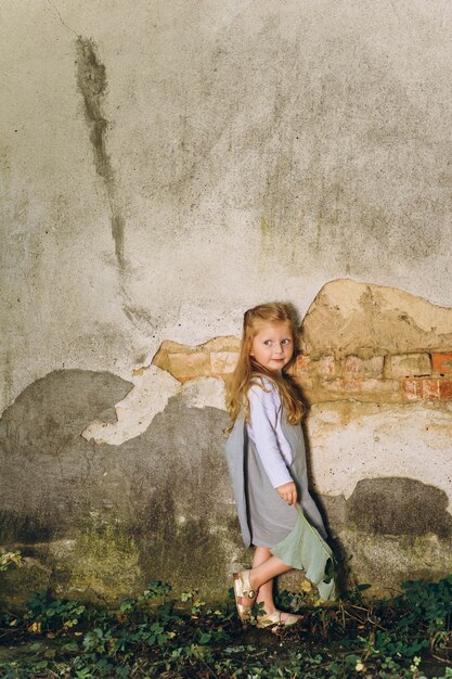 bella ragazza in un abito grigio con una foglia in mano in piedi sull&#39;erba sullo sfondo del muro