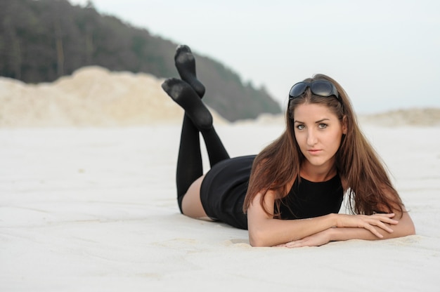 Bella ragazza in un abito nero sulla spiaggia. Moda ritratto di donna abbronzata sulla spiaggia del mare