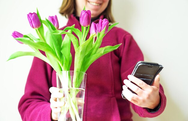 Bella ragazza in un'accogliente giacca viola con tulipani magenta sorride e si fa un selfie sul suo telefono