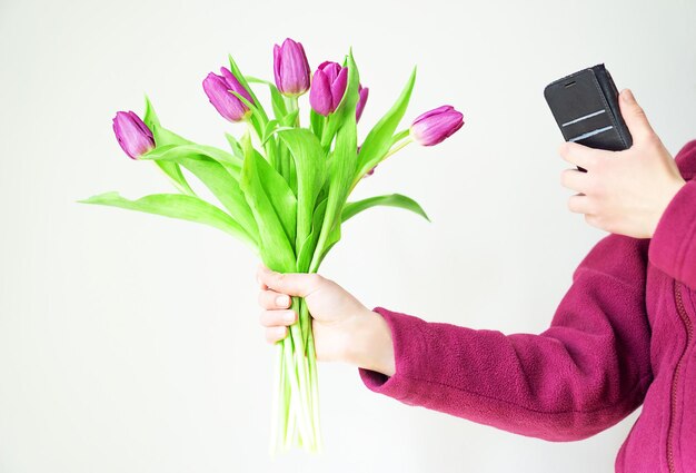 Bella ragazza in un'accogliente giacca viola con tulipani magenta sta scattando una foto sul suo telefono.