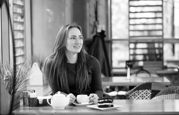 Bella ragazza in un caffè seduto e bevendo tè con dessert