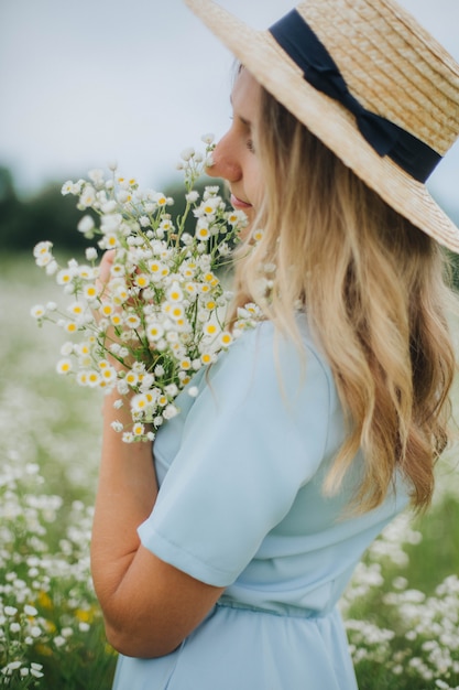 bella ragazza in un campo di margherite. ragazza con un cappello di paglia e un vestito blu. campo di camomilla in estate