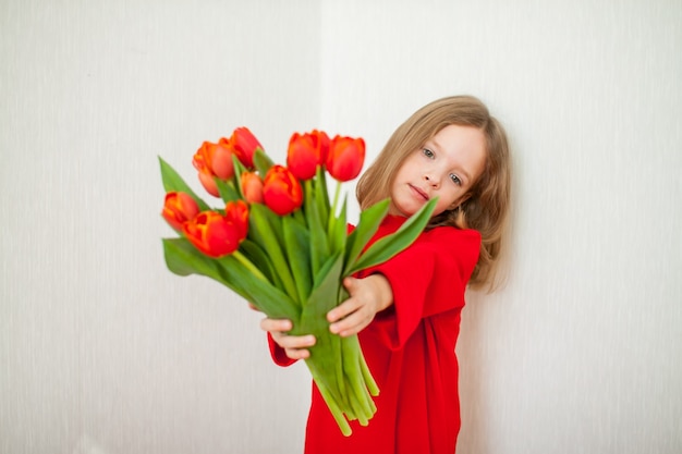 Bella ragazza in un dolcevita rosso brillante che tiene un mazzo di tulipani rossi. Foto di alta qualità