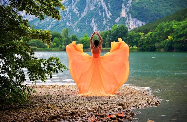 Bella ragazza in un fantastico vestito arancione svolazzante con la laguna e le montagne sullo sfondo