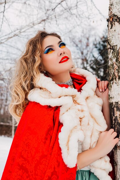 Bella ragazza in un mantello rosso nella foresta d'inverno