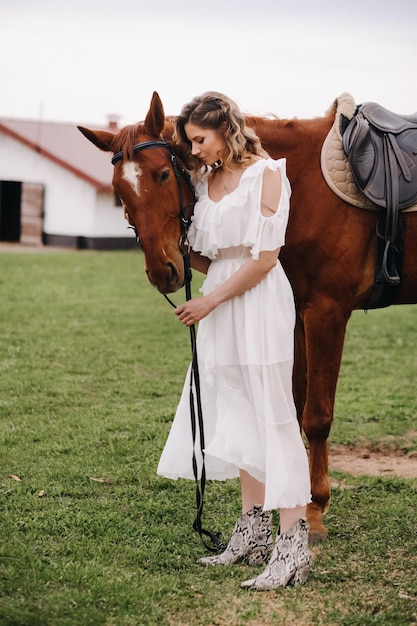 Bella ragazza in un prendisole bianco accanto a un cavallo in un vecchio ranch