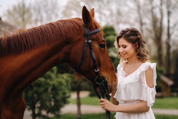 Bella ragazza in un prendisole bianco accanto a un cavallo in un vecchio ranch