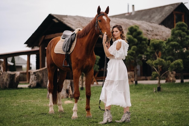 Bella ragazza in un prendisole bianco accanto a un cavallo in un vecchio ranch