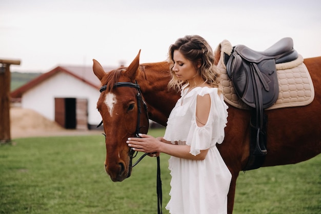 Bella ragazza in un prendisole bianco accanto a un cavallo in un vecchio ranch