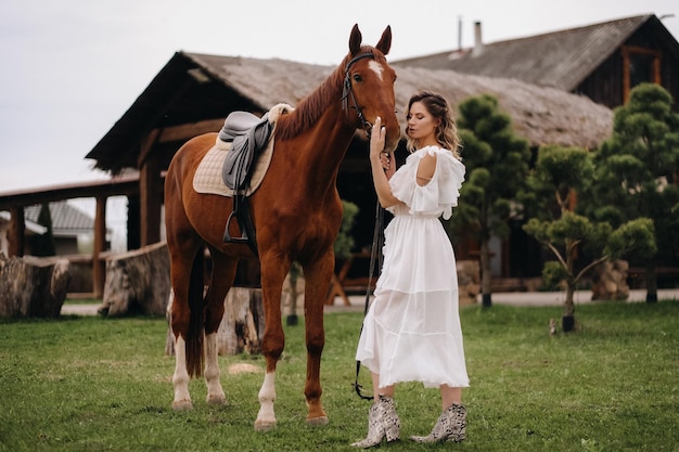 Bella ragazza in un prendisole bianco accanto a un cavallo in un vecchio ranch