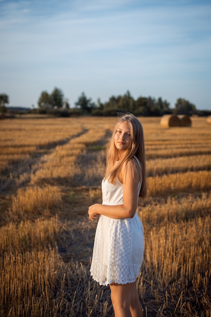 Bella ragazza in un vestito bianco chiaro che fa una passeggiata all'aperto sul campo dopo il raccolto