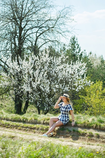 Bella ragazza in un vestito che cammina nella foresta primaverile dove fioriscono gli alberi